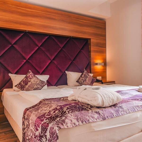Doppelbett im Apartment der Arkona Strandresidenzen Binz mit gemütlicher Beleuchtung und lila Samt-Kopfteil