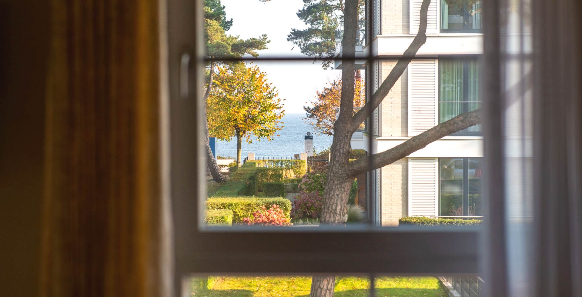 Blick aus dem Apartmentfenster der Arkona Strandresidenzen auf die Ostsee mit Garten und herbstlichen Bäumen in Binz