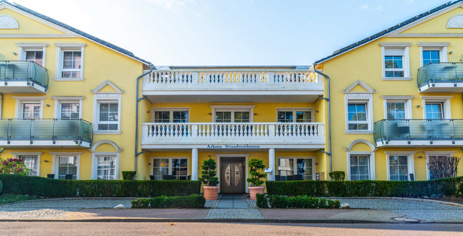 Die gelb-weiße Fassade der Arkona Strandresidenzen bei sonnigem Wetter an der Binzer Strandpromenade.